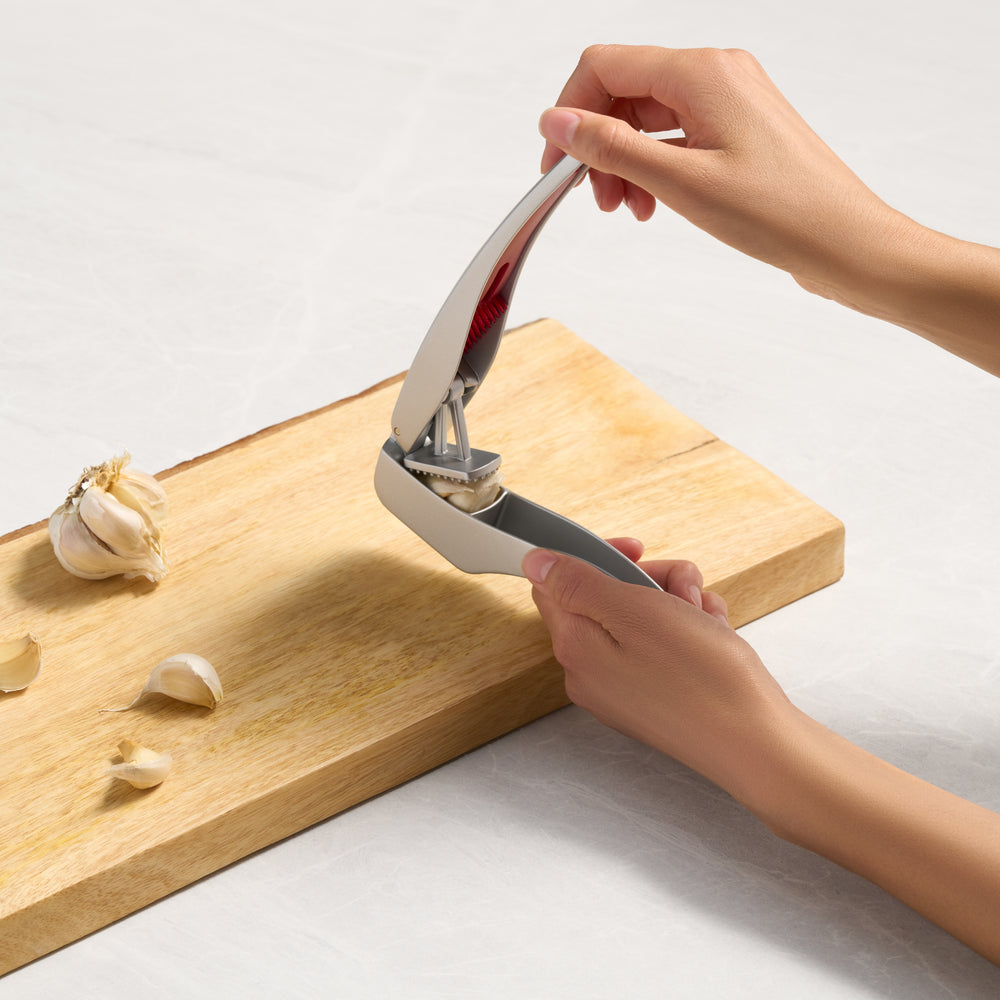 The Zyliss Susi 3 Garlic Press, made of stainless steel with an ergonomic handle and red accent, is shown closed on a white background. It’s dishwasher safe for easy cleaning.