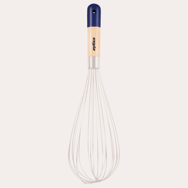 The Zyliss Beech Wood Balloon Whisk has stainless steel wires, a beech wood handle with a blue tip, small hanging hole, and printed logo. Shown on a plain white background.