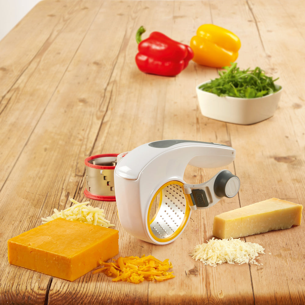 The Zyliss All Cheese Grater features stainless steel blades, interchangeable drums, a white handheld design, black grip, red drum rim, and gray push button for easy grating.