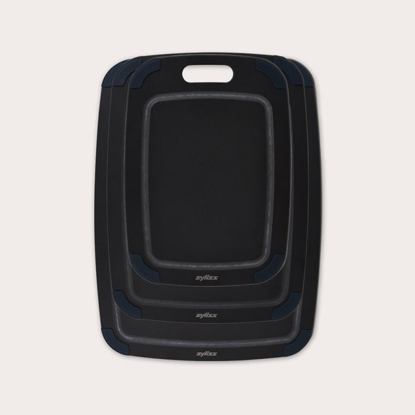 The Zyliss Wood Fibre Cutting Boards set features three nested black boards in different sizes, each with a handle slot and dark gray corner grips, made from eco-friendly recycled wood fibres and shown on a light background. #set of 3