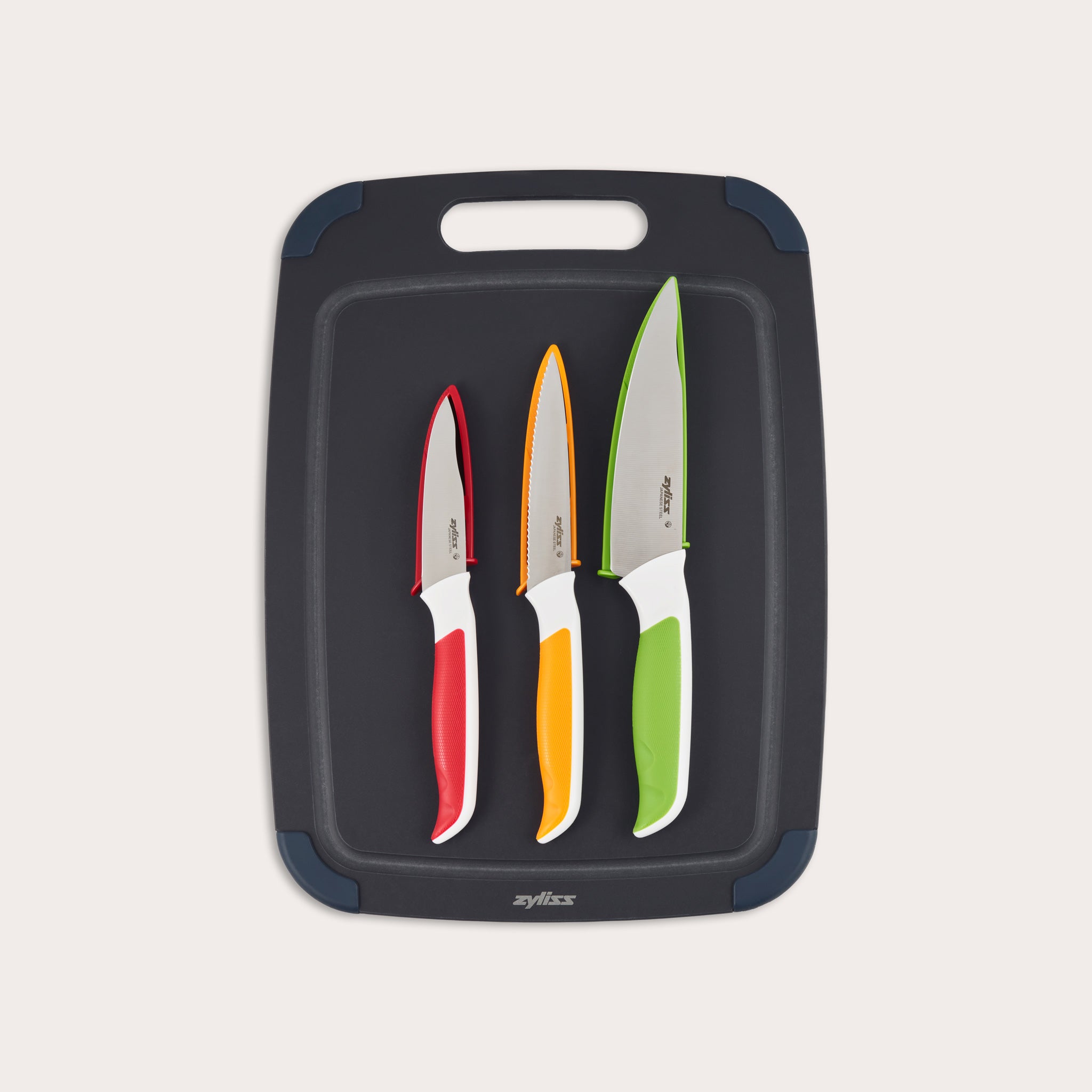 A Zyliss 4 Piece Wood Fibre Chopping Board & Knife Set features three kitchen knives with red, orange, and green handles, neatly displayed on a sleek black chopping board.