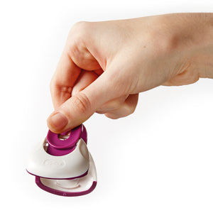 A hand holds a Zyliss Clip-All Bag Clip (white and purple), pinching the top to open its jaws—this kitchen essential helps prevent food spillage. Shown in mixed sizes, isolated on a white background.