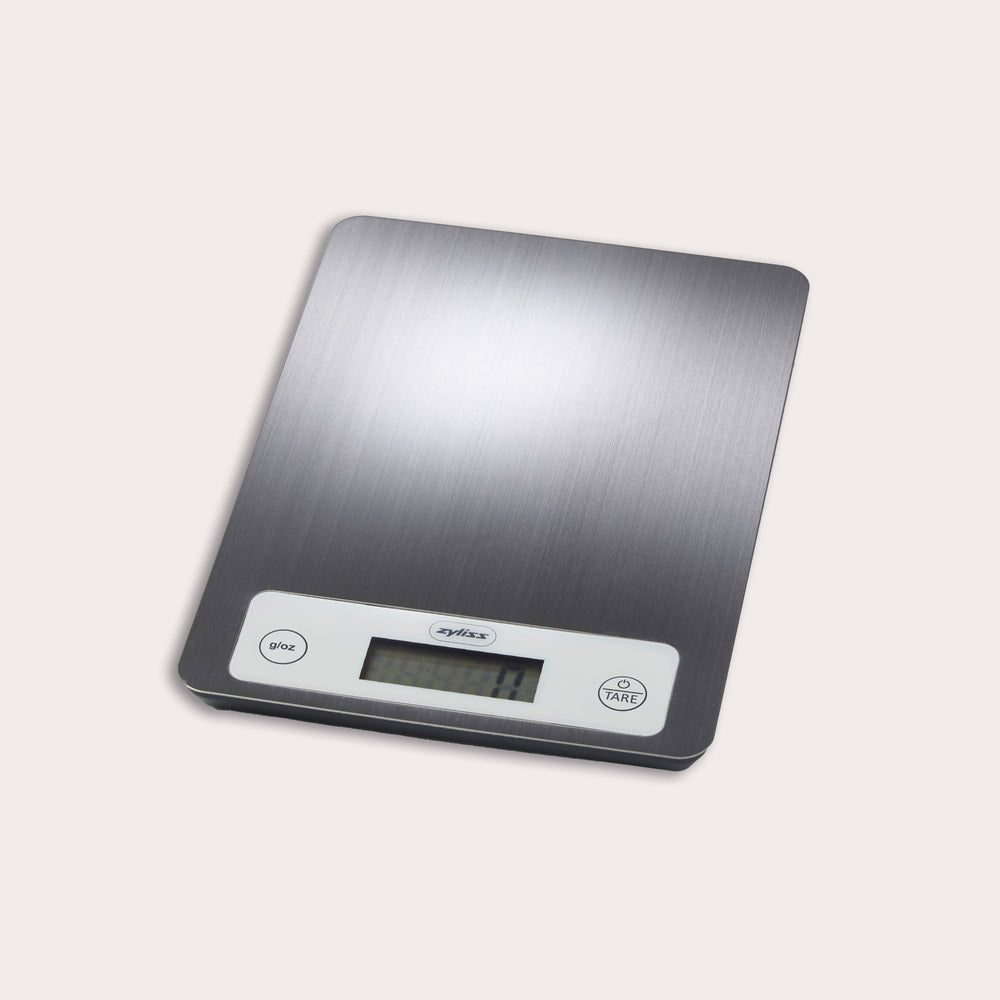 The Zyliss Electronic Measuring Scale features a brushed metal surface, white control panel with digital display, and two buttons (give and tare), making it perfect for precise cooking on any countertop.