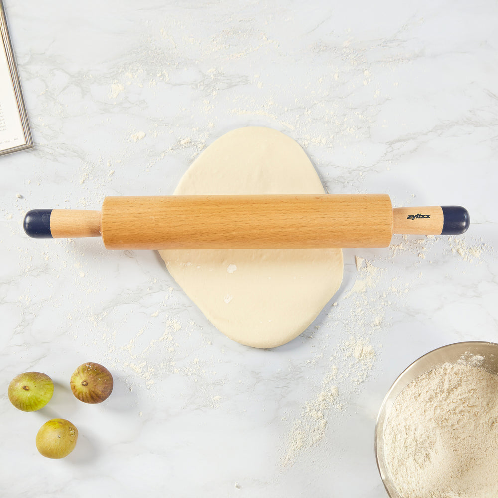 A Zyliss Beech Wood Rolling Pin with blue comfort-grip handles rests horizontally on a light background, showcasing the brand name for an essential tool in any kitchen.