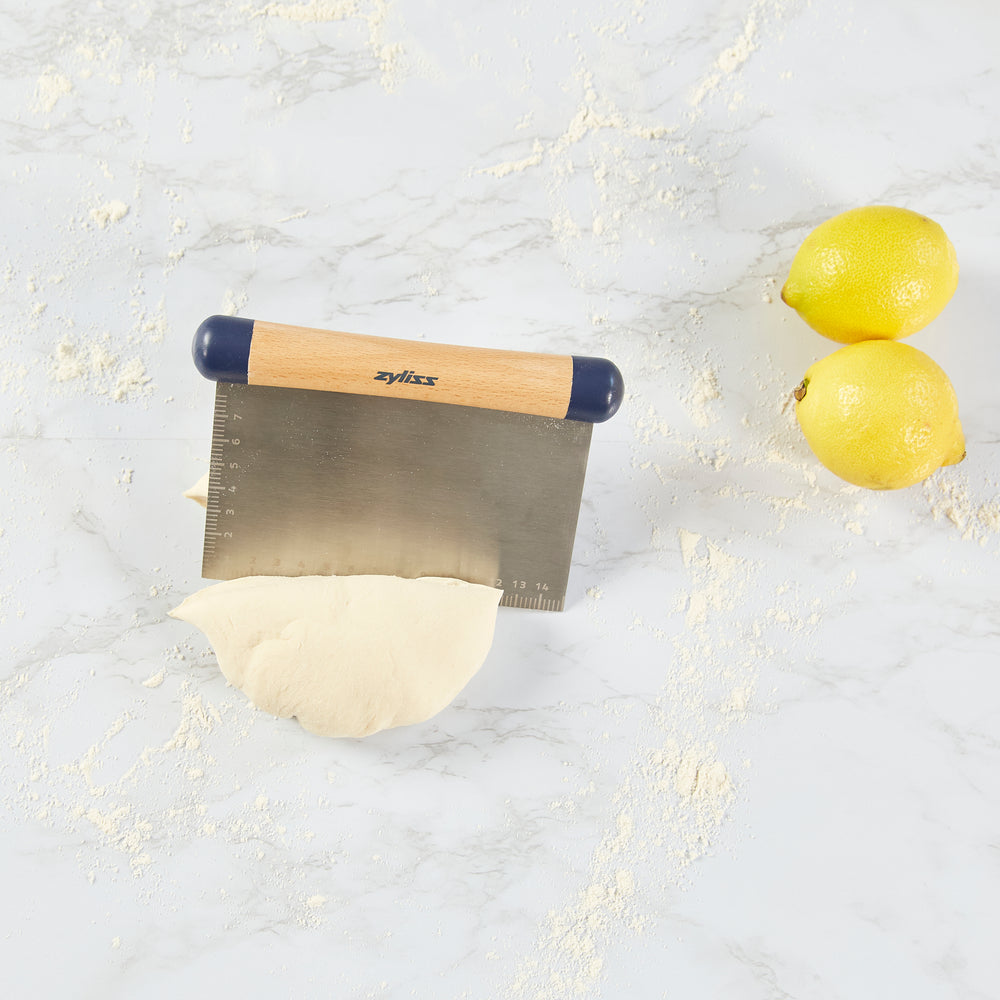 The Zyliss Beech Wood Bench Scraper features a beech wood handle, blue plastic ends, and a metal blade with an etched ruler—a versatile tool for baking tasks.