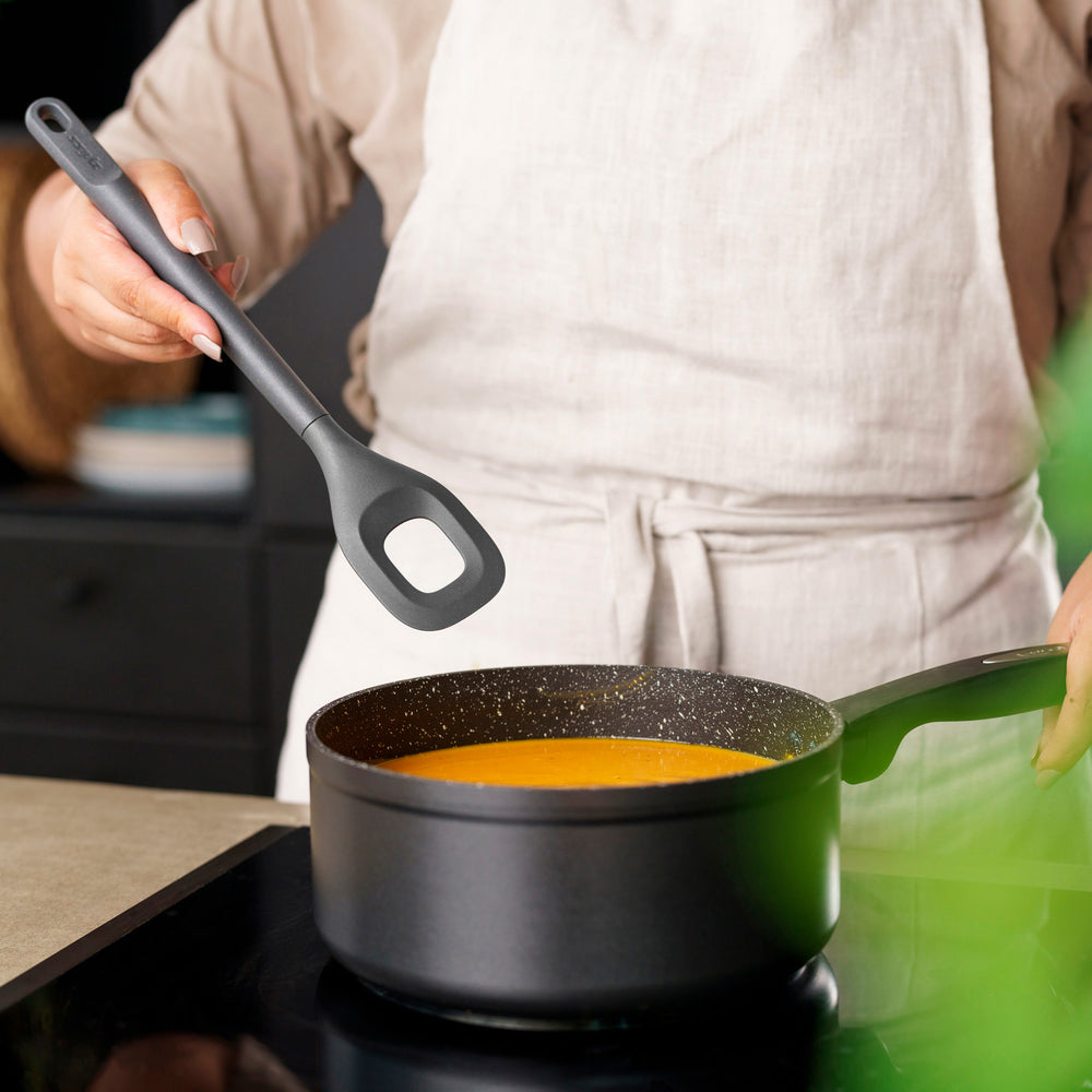 The Zyliss Square Mixing Spoon is a gray, heat-resistant silicone utensil with a long handle and a rectangular hole in the head. Shown on a plain light background, its dishwasher safe for easy cleaning.
