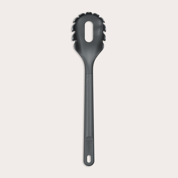 The Zyliss Spaghetti Server is a black, heat-resistant utensil with a long handle and slotted, rounded head featuring prongs for ideal portion control, shown isolated on a light background.