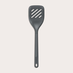 The Zyliss Slotted Turner, shown in black with three diagonal slots and an ergonomic handle, features a heat-resistant design for safe cooking or flipping food. Displayed against a plain white background.