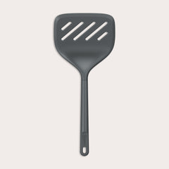 A Zyliss Turner XL slotted spatula in black, featuring a wide square head with three diagonal slots, ergonomic handle, and heat-resistant design is displayed against a plain light background.