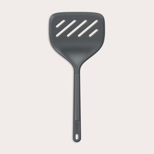A Zyliss Turner XL slotted spatula in black, featuring a wide square head with three diagonal slots, ergonomic handle, and heat-resistant design is displayed against a plain light background.