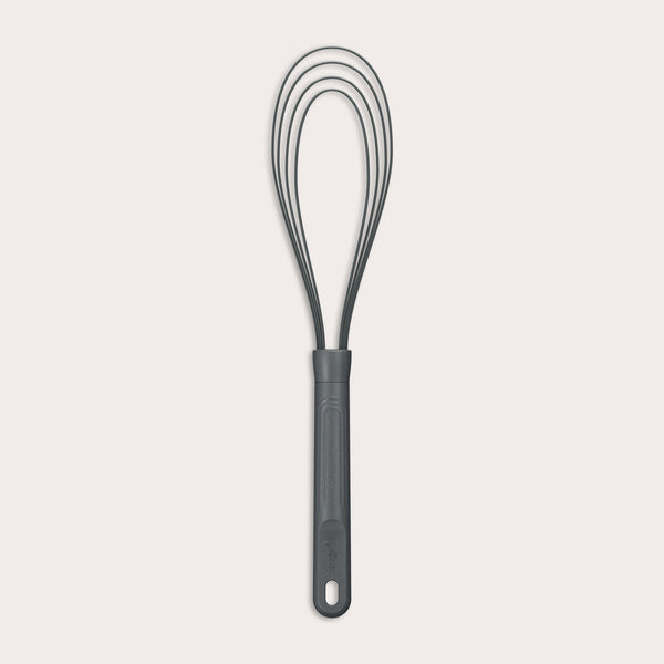 The Zyliss Flat Whisk Silicone features a black, heat-resistant silicone design with a long handle and looped wires, displayed on a plain light background.