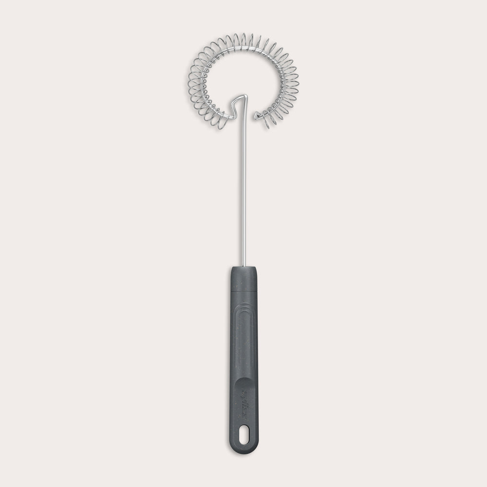 The Zyliss Gravy Whisk features a metal spiral and a dark plastic handle with a hanging hole. It is heat-resistant and shown against a plain light background.