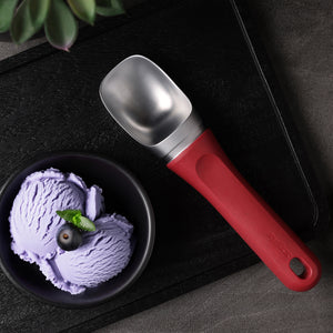 #berry A black bowl with two scoops of purple ice cream, topped with a blueberry and mint, is placed beside the Zyliss Ice Cream Scoop, which features an eco-friendly handle, on a dark tray.