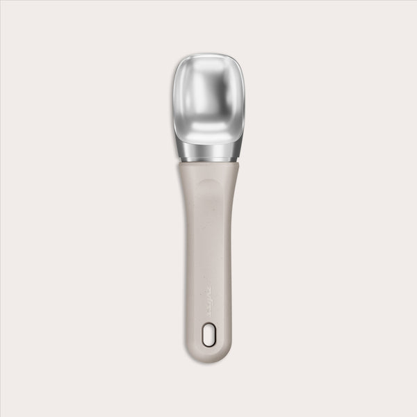 #naturalbeige The Zyliss Ice Cream Scoop features a wide, flat silver scoop and an eco-friendly beige handle made from sustainable wheat straw, with a small hole near the end, shown centered on a plain light background.