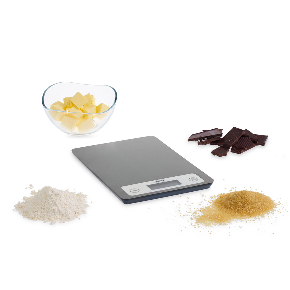 The Zyliss Electronic Measuring Scale features a brushed metal surface, white control panel with digital display, and two buttons (give and tare), making it perfect for precise cooking on any countertop.