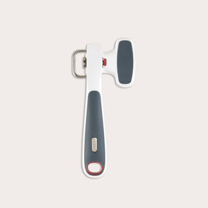 The Zyliss Safe Edge Can Opener has an ergonomic design, white and dark gray handle with red accents, and a metal turning mechanism, displayed against a plain light background.