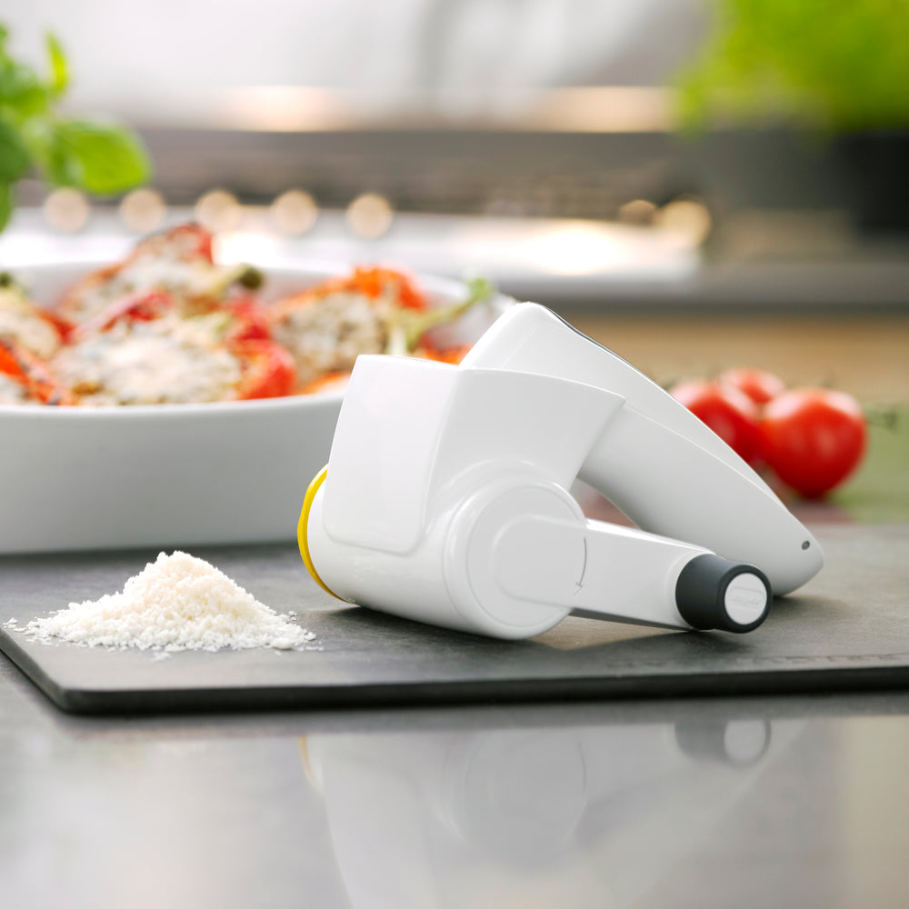 The Zyliss Classic Cheese Grater features a white and gray ergonomic handle, stainless steel drum, crank handle, and cheese compartment for comfortable grating.