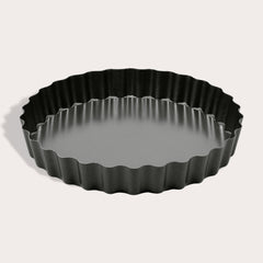 The Zyliss Non-Stick Tart Pan is round and black with fluted edges, a flat bottom, and a removable base—ideal for baking tarts or quiches. The empty pan is displayed on a light background.