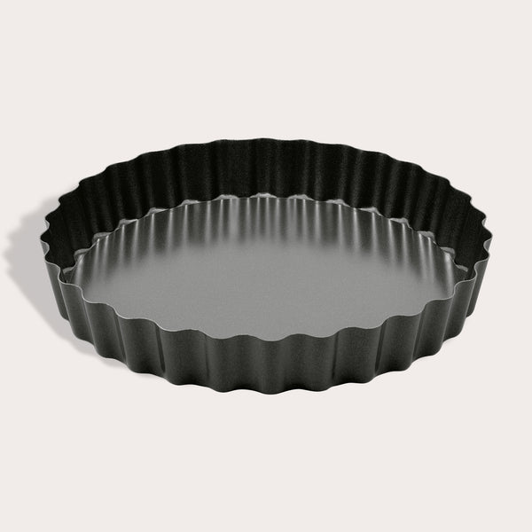 The Zyliss Non-Stick Tart Pan is round and black with fluted edges, a flat bottom, and a removable base—ideal for baking tarts or quiches. The empty pan is displayed on a light background.
