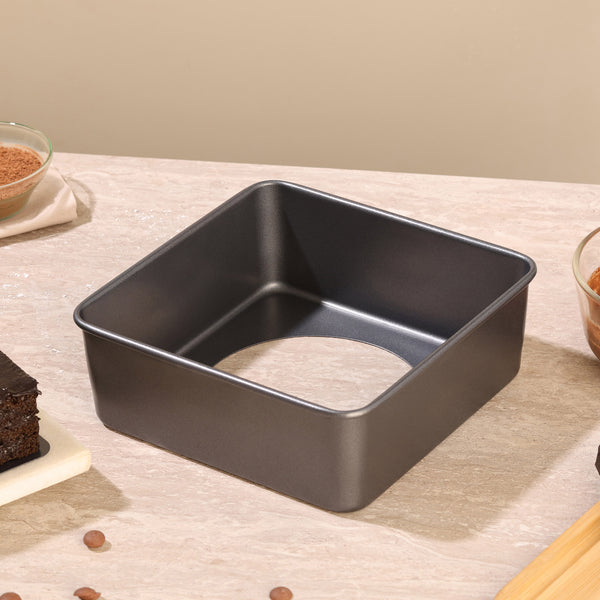 A Zyliss Non-Stick Base Square Pan 20cm/8" with a removable base sits on a beige countertop, surrounded by bowls and pieces of chocolate cake.