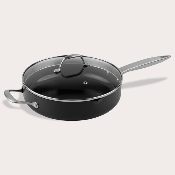 A Zyliss Ultimate Pro Ceramic Saute Pan With Lid, featuring a black nonstick surface, glass lid, long metal handle, and short helper handle, is displayed against a plain light background. 