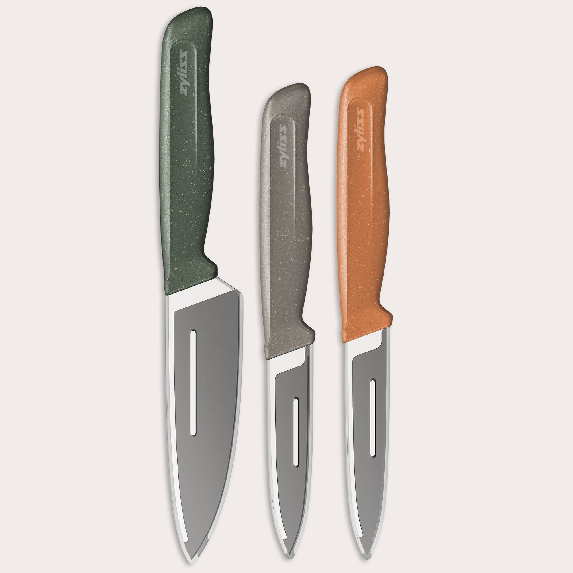 The Zyliss 3 Piece Knife Set includes chef and paring knives with green, gray, and orange handles, each with a protective sheath, displayed side by side on a light background for a vibrant kitchen look.