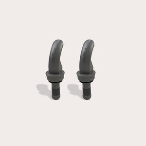 Two black, curved Zyliss Bottle Stopper 2 Piece Set items with a matte finish are displayed upright on a light beige background, featuring sleek designs that resemble wireless earbuds and small brand markings on their surfaces.