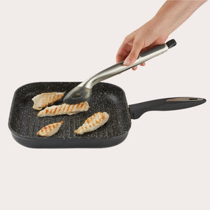 A hand uses tongs to lift grilled chicken from the Zyliss Cacio e pepe bundle’s black, square nonstick grill pan with a handle.