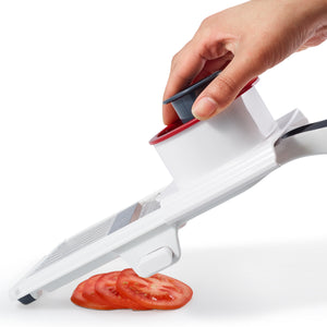 A hand uses the Zyliss Easy Control Handheld Slicer, which features a white and red design, to cut uniform tomato slices; several even slices are visible below the slicer. Its adjustable thickness feature allows for precise slicing, and this tool is dishwasher safe for effortless cleanup.
