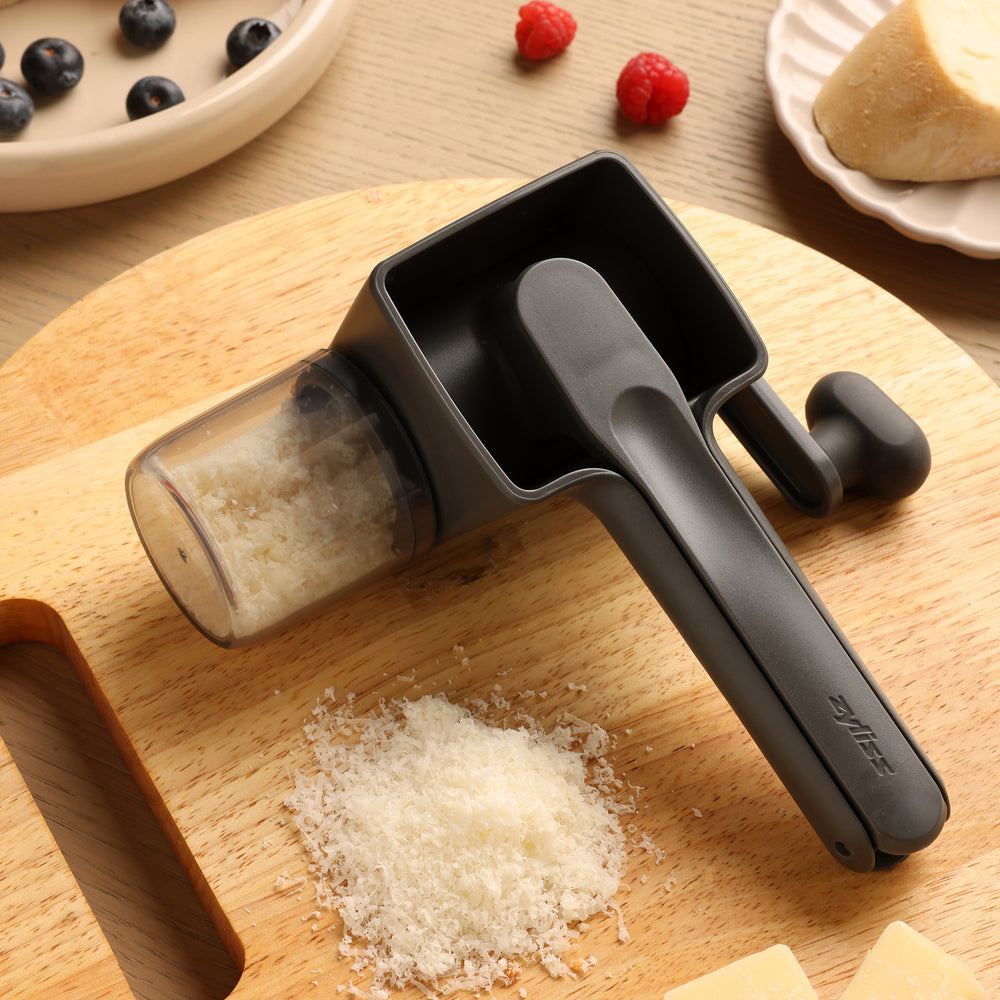 The Zyliss Professional Rotary Cheese Grater Set, in black, features an ergonomic crank, transparent detachable container, and visible grater drum with the handle extended.