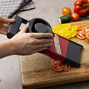 Hands slicing a tomato using a Zyliss 4-in-1 Slicer and Grater with Interchangeable Blades over a wooden cutting board.