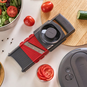 A Zyliss 4-in-1 Slicer and Grater with Interchangeable Blades surrounded by sliced tomatoes, a bowl of salad, and a cucumber on a kitchen surface.