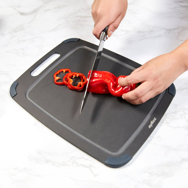 A person slices a red bell pepper with a knife on a Zyliss Wood Fibre Cutting Board, made from recycled wood fibres, set on a white countertop. #Medium