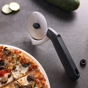 A Zyliss Pizza & Pastry Cutter with a black handle sits on a gray surface next to a partially visible pizza and sliced zucchini.