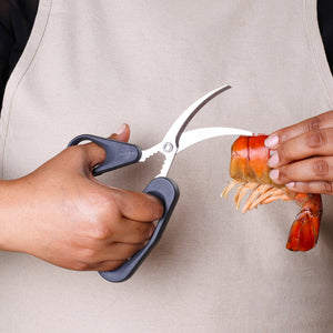 A person uses Zyliss Seafood Scissors to cut open a large shrimp shell while wearing a beige apron—perfect for effortless shellfish preparation.