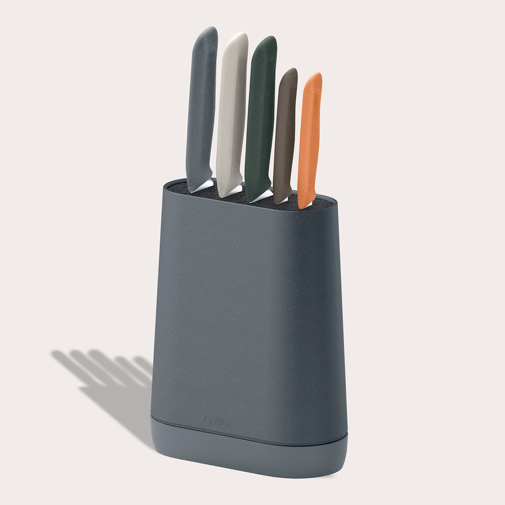 The Zyliss 6 Piece Universal Knife Block in dark gray holds five stainless steel knives with ergonomic handles in orange, green, white, light gray, and dark gray, shown against a plain light background.