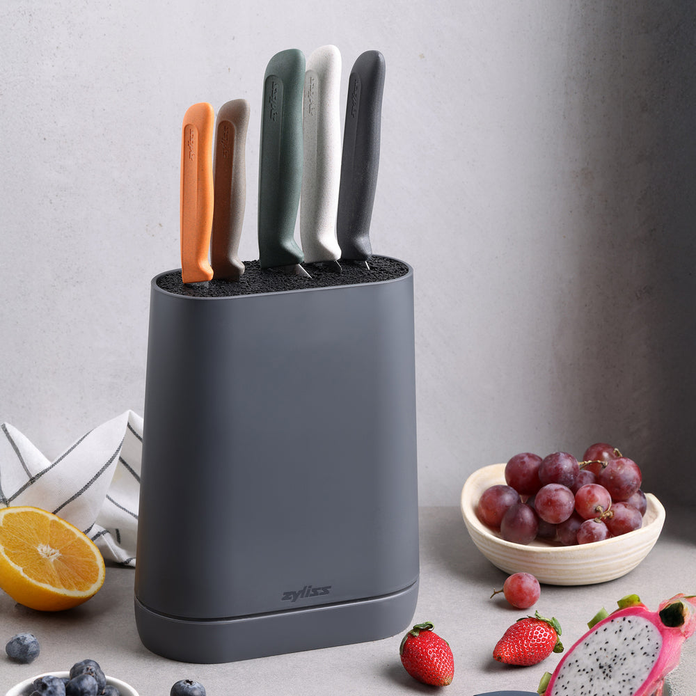 The Zyliss 6 Piece Universal Knife Block in dark gray holds five stainless steel knives with ergonomic handles in orange, green, white, light gray, and dark gray, shown against a plain light background.