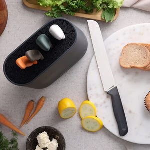 A Zyliss 6 Piece Universal Knife Block with four colorful stainless steel knives is displayed beside a serrated bread knife, an ergonomic handle, and a marble cutting board holding sliced bread, carrots, squash, and lettuce.