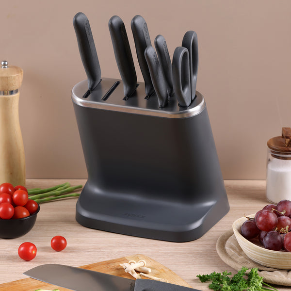 A Zyliss 8-Piece Knife Block with Japanese stainless steel knives is on the counter, surrounded by a pepper grinder, cherry tomatoes, grapes, green beans, salt, and chopped herbs.