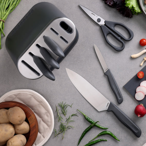 The Zyliss 8-Piece Knife Block includes sustainable knives, kitchen scissors, and a cutting board with chopped veggies, green chilies, fresh herbs, potatoes in a bowl, plus a potholder—all on a gray countertop.