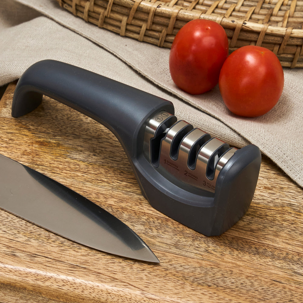 The Zyliss Knife Sharpener features a gray ergonomic handle and three sharpening slots for kitchen blades and serrated edges, displayed on a plain, light background.