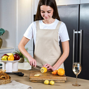 In a modern kitchen, a woman in a beige apron uses the Zyliss Comfort Pro Serrated Paring Knife 11.5cm to slice a lemon on a wooden cutting board, with oranges, apples, white wine, and bread arranged nearby on the counter.
