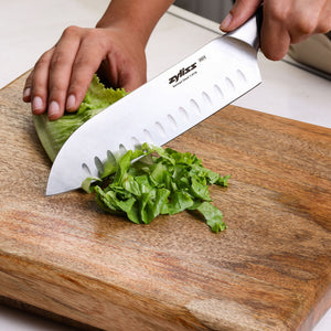 A hand slices green lettuce with a sharp Zyliss Comfort Pro Chef + Santoku Knife Set on a wooden cutting board.