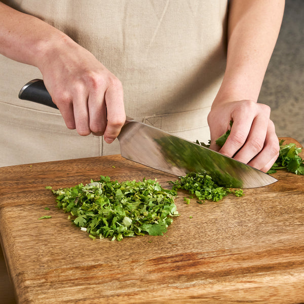 A person chops fresh green herbs on a wooden cutting board with the Zyliss Comfort Pro Chef Knife 19cm / 7½", known for its ergonomic handle.