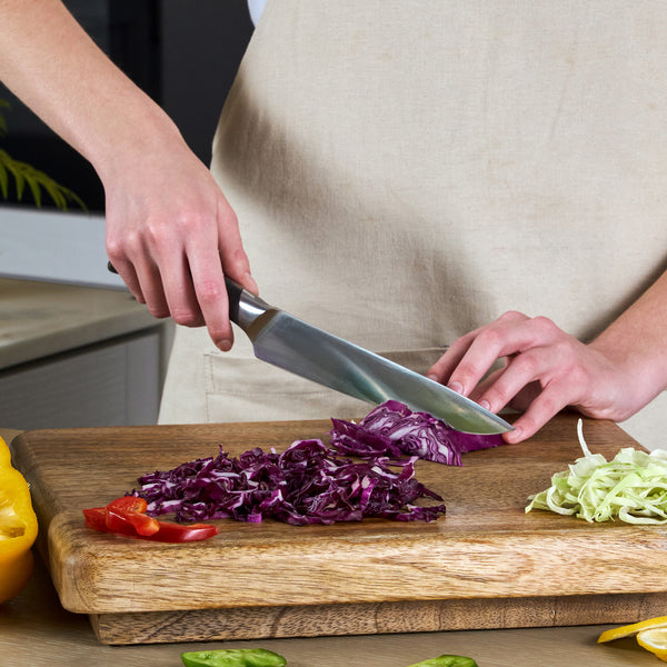 A person uses the Zyliss Comfort Pro Carving Knife 20cm/8" with an ergonomic handle to slice purple cabbage on a wooden cutting board, which also holds chopped green cabbage and red and yellow bell pepper pieces.