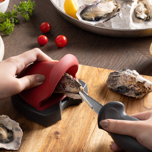 Hands using the zyliss oyster shucking set to open an oyster on a wooden board.