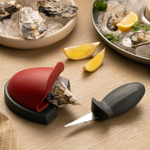 zyliss oyster shucking set with an oyster in the holder and the knife beside a plate of oysters.