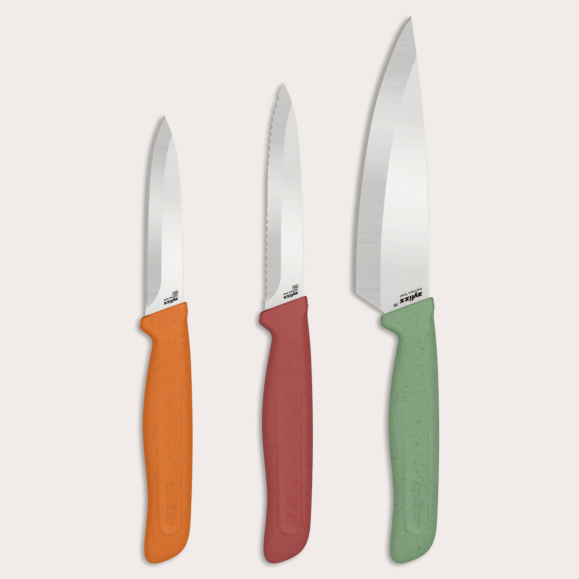 The Zyliss Classic 3-Piece Paring & Utility Knife Set features stainless steel knives with colorful orange, red, and green handles. Upright against a light background, the center utility knife is serrated; the paring knives have smooth blades.