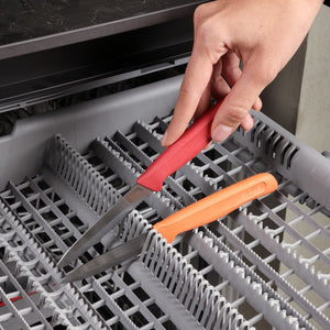 A hand places two Zyliss Classic 2-Piece Paring Knives, featuring ergonomic handles and stainless steel blades, blade-side down into the dishwasher's cutlery rack.