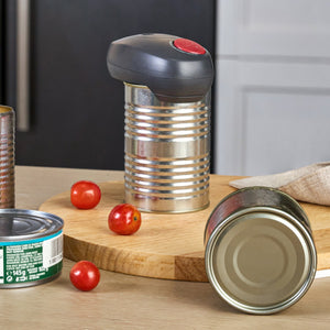 A Zyliss Electronic Can Opener with One-Touch Start/Stop attached to the top of a metal can on a wooden cutting board with cherry tomatoes nearby.
